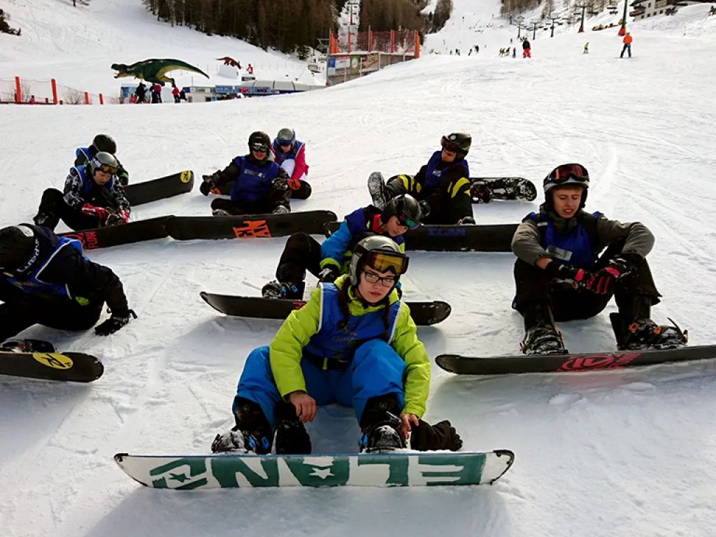 Jugendliche sitzen mit Snowboards im Schnee.